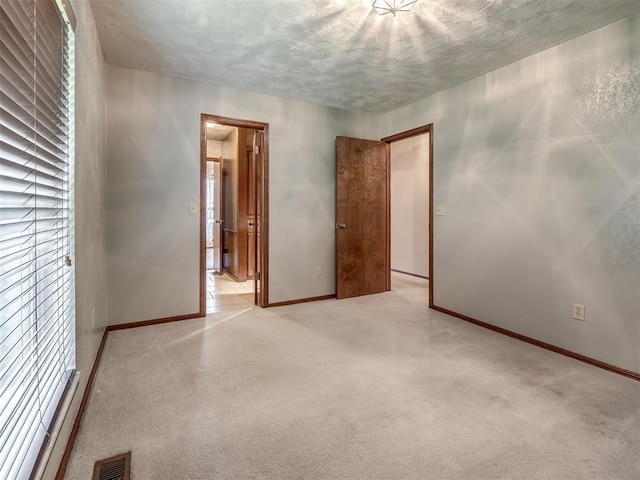 spare room with baseboards, light colored carpet, a textured ceiling, and visible vents