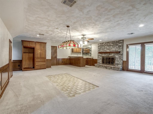 unfurnished living room with light colored carpet, ceiling fan, visible vents, and wainscoting