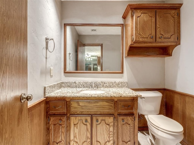 half bathroom with vanity, wainscoting, wooden walls, and toilet