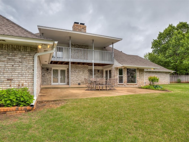 rear view of house featuring a balcony, a chimney, brick siding, a patio area, and a yard