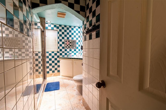 bathroom with tile patterned flooring, toilet, tile walls, and a tile shower