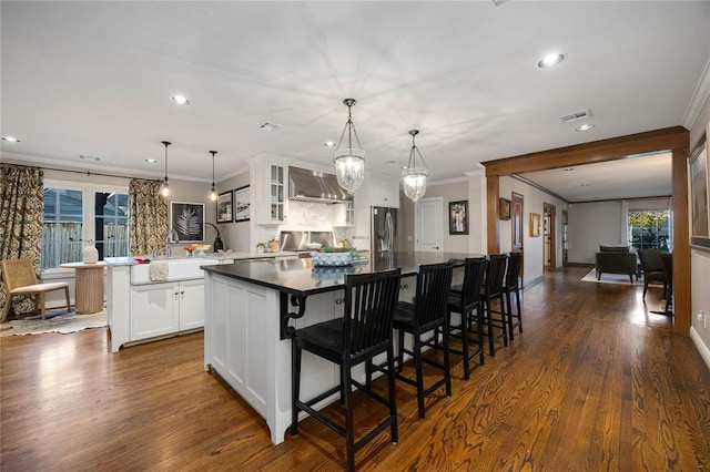 kitchen featuring dark wood-type flooring, white cabinets, wall chimney range hood, kitchen peninsula, and stainless steel refrigerator