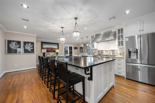 kitchen with white cabinets, wall chimney range hood, a breakfast bar area, and appliances with stainless steel finishes