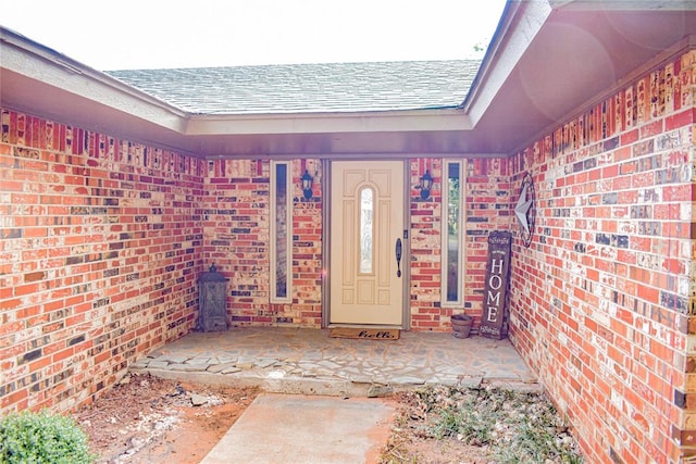 property entrance featuring brick siding and a shingled roof