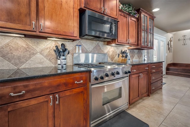 kitchen featuring decorative backsplash, stainless steel gas range oven, dark stone countertops, and light tile patterned flooring