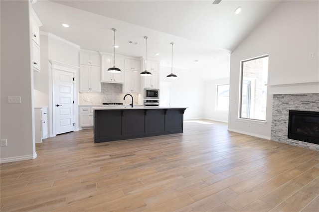 kitchen with built in microwave, white cabinetry, decorative light fixtures, vaulted ceiling, and a center island with sink