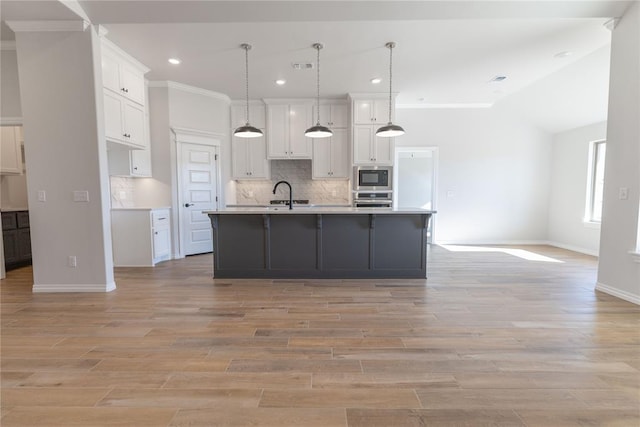 kitchen with hanging light fixtures, white cabinets, a kitchen island with sink, and built in microwave