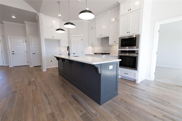 kitchen with built in microwave, white cabinetry, an island with sink, stainless steel oven, and decorative backsplash