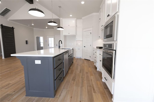 kitchen with sink, white cabinets, a barn door, a large island with sink, and stainless steel appliances