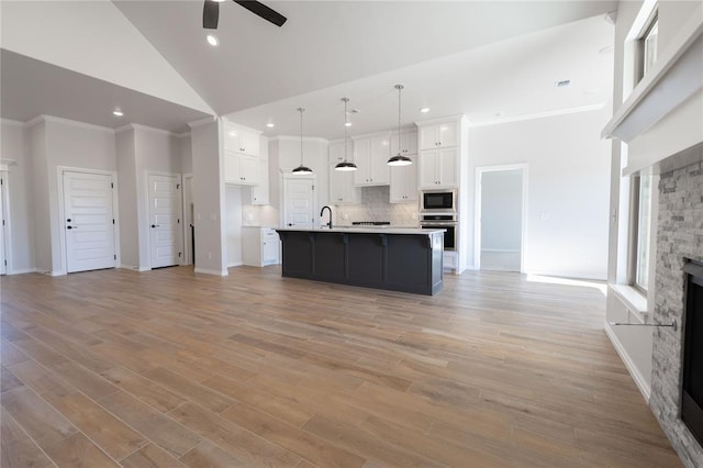 kitchen with high vaulted ceiling, white cabinets, appliances with stainless steel finishes, and an island with sink