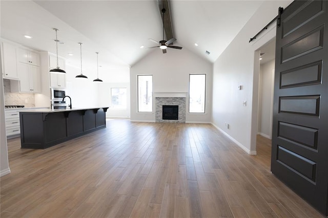 kitchen featuring hardwood / wood-style flooring, white cabinetry, a barn door, black microwave, and an island with sink