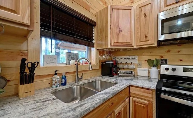 kitchen with appliances with stainless steel finishes, light brown cabinetry, light stone counters, wooden walls, and sink