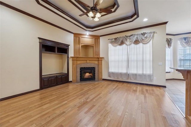 unfurnished living room featuring light wood-type flooring, a tray ceiling, ceiling fan, crown molding, and a tiled fireplace