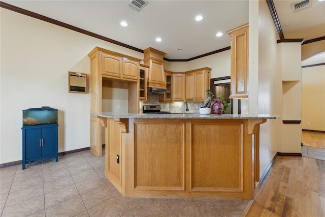 kitchen with kitchen peninsula, light stone counters, stainless steel range, crown molding, and a breakfast bar area