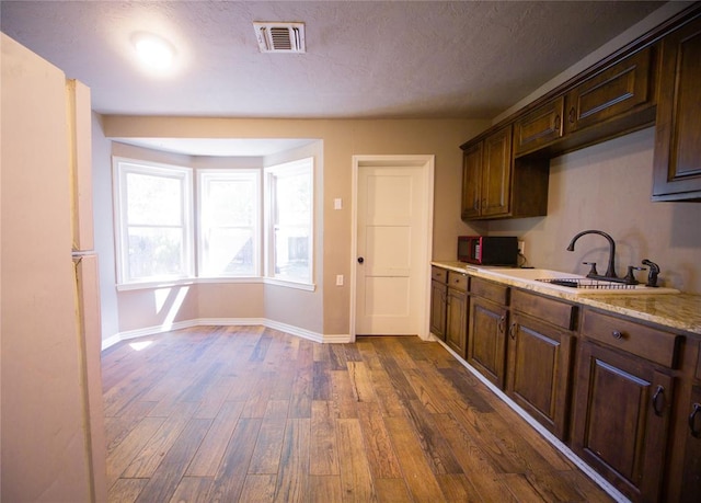 kitchen featuring sink, dark brown cabinetry, light stone countertops, and dark wood-type flooring