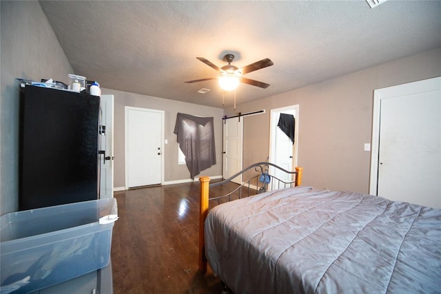 bedroom featuring ceiling fan, dark hardwood / wood-style floors, a barn door, and a textured ceiling