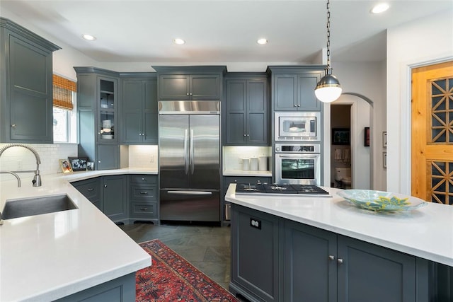 kitchen featuring built in appliances, pendant lighting, sink, and tasteful backsplash