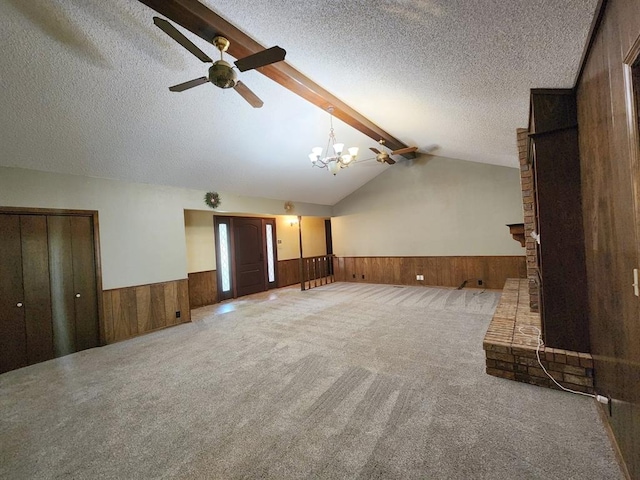 unfurnished living room with vaulted ceiling with beams, wood walls, carpet floors, and a textured ceiling