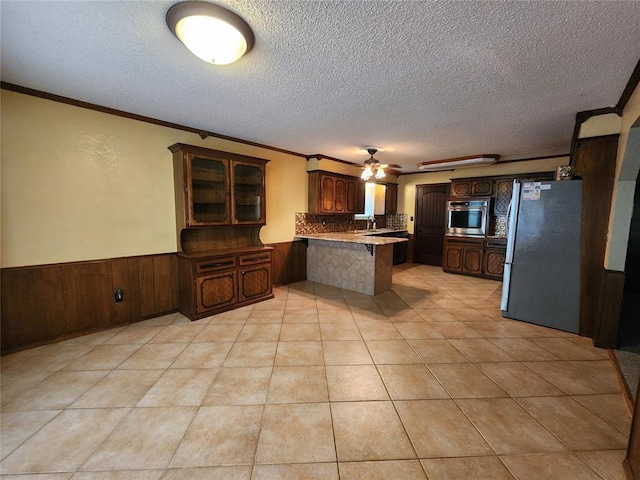 1116 Reid Cir, Seminole, OK 74868 - kitchen featuring stainless steel appliances, a peninsula, ceiling fan, a textured ceiling, and a wainscoted wall