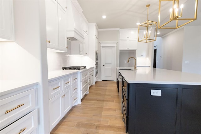 kitchen featuring decorative light fixtures, white cabinets, backsplash, a center island with sink, and light hardwood / wood-style flooring