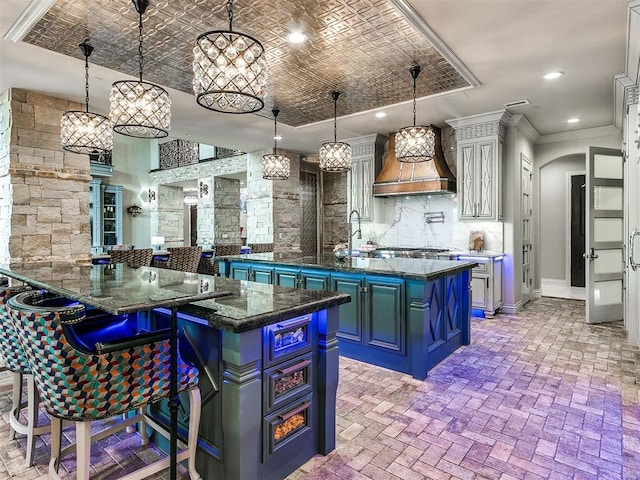 kitchen with a center island, hanging light fixtures, crown molding, dark stone counters, and custom exhaust hood