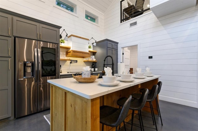 kitchen with gray cabinets, an island with sink, stainless steel refrigerator with ice dispenser, and high vaulted ceiling