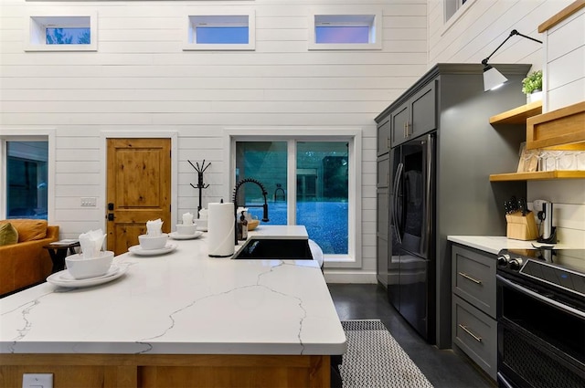 kitchen with gray cabinets, a kitchen island with sink, light stone counters, and wood walls