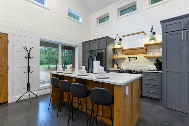 kitchen featuring a breakfast bar, a kitchen island with sink, high vaulted ceiling, gray cabinets, and appliances with stainless steel finishes