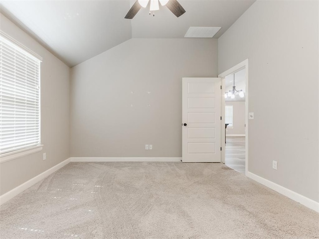 empty room featuring ceiling fan with notable chandelier, carpet floors, and vaulted ceiling