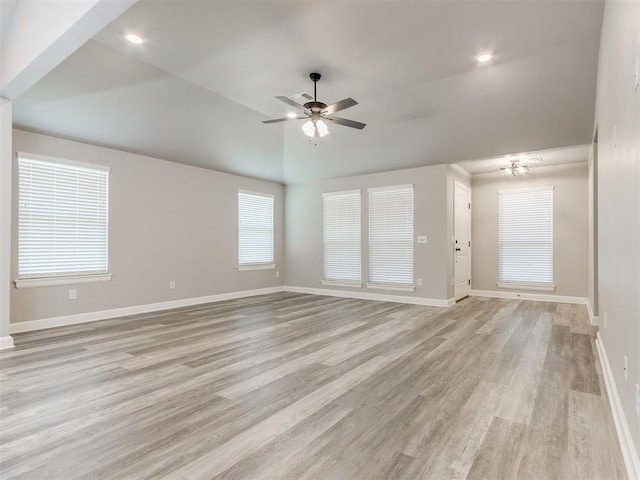 unfurnished living room featuring ceiling fan with notable chandelier, light hardwood / wood-style flooring, and vaulted ceiling