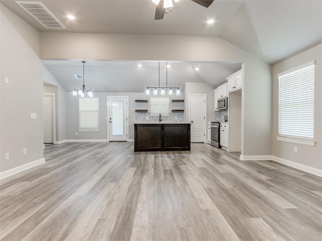 kitchen featuring white cabinets, vaulted ceiling, light wood-type flooring, an island with sink, and appliances with stainless steel finishes