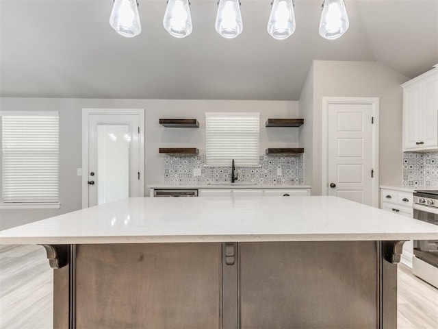 kitchen with a large island, sink, decorative backsplash, white cabinets, and appliances with stainless steel finishes