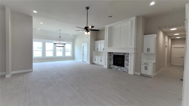 unfurnished living room with ceiling fan, a stone fireplace, lofted ceiling, and light hardwood / wood-style flooring