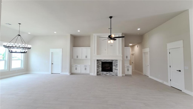 unfurnished living room featuring a fireplace, ceiling fan with notable chandelier, and high vaulted ceiling