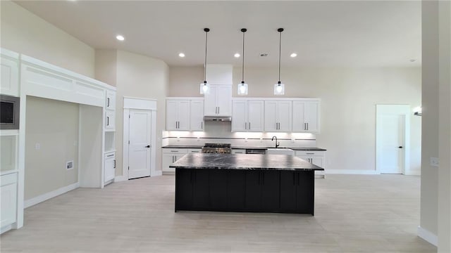 kitchen with white cabinets, sink, hanging light fixtures, stainless steel stove, and a kitchen island