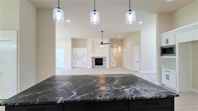 kitchen featuring white cabinetry, stainless steel microwave, a kitchen island, and hanging light fixtures