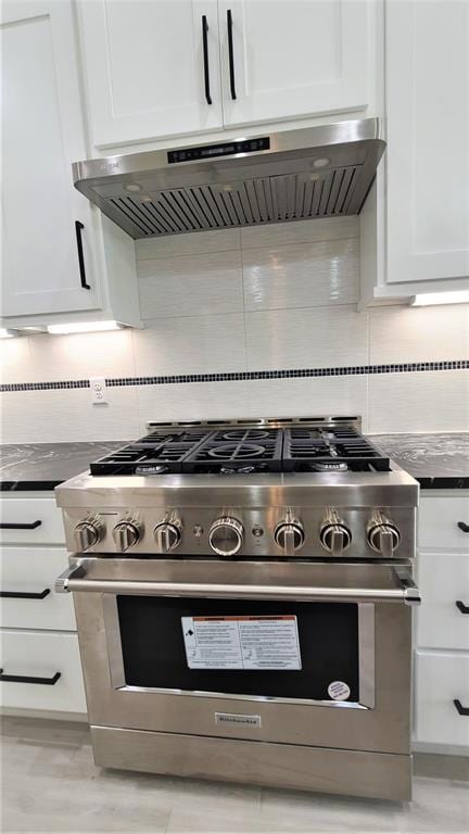 kitchen featuring ventilation hood, white cabinetry, stainless steel stove, and tasteful backsplash