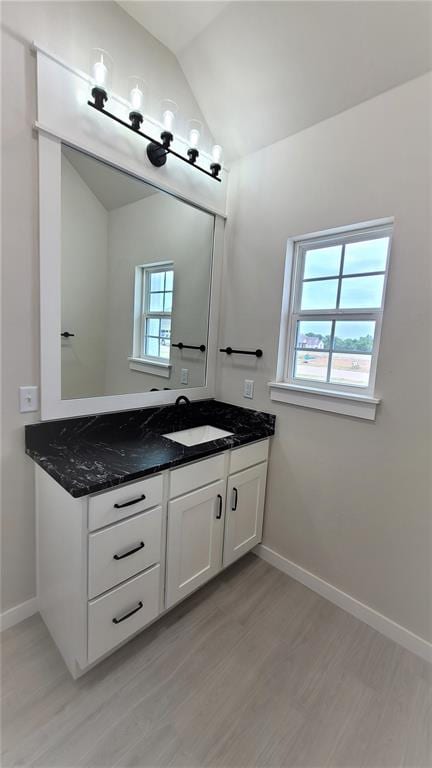 bathroom featuring hardwood / wood-style flooring, vanity, a healthy amount of sunlight, and vaulted ceiling