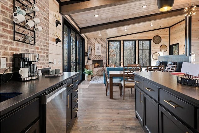 kitchen featuring a brick fireplace, brick wall, lofted ceiling with beams, hardwood / wood-style flooring, and dishwasher