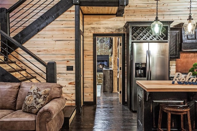 interior space with decorative light fixtures, stainless steel fridge with ice dispenser, and wooden walls