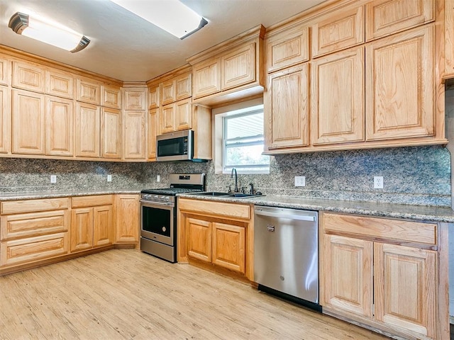 kitchen featuring light stone countertops, sink, appliances with stainless steel finishes, and light hardwood / wood-style flooring