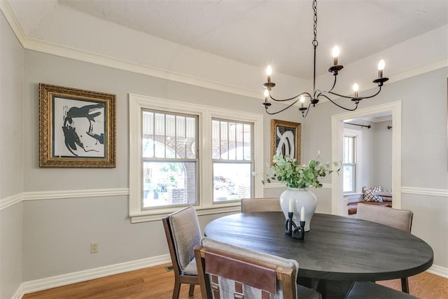 dining space with hardwood / wood-style floors, plenty of natural light, ornamental molding, and a notable chandelier