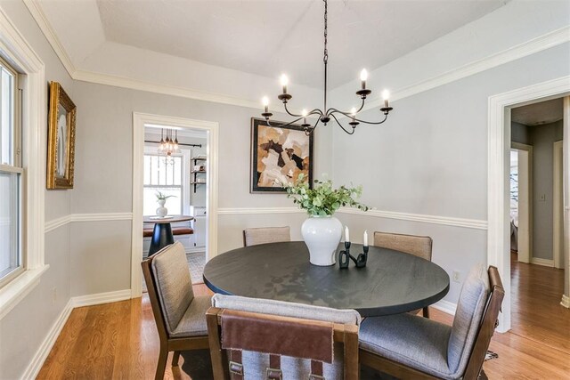 dining space with hardwood / wood-style flooring, a notable chandelier, a raised ceiling, and ornamental molding