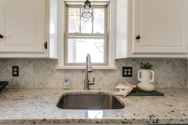 kitchen featuring tasteful backsplash, light stone counters, sink, and pendant lighting