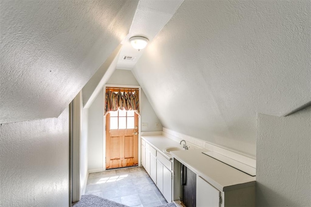 additional living space with a textured ceiling, lofted ceiling, and sink