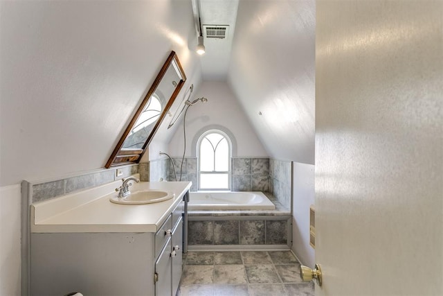 bathroom featuring tiled bath, vanity, and vaulted ceiling