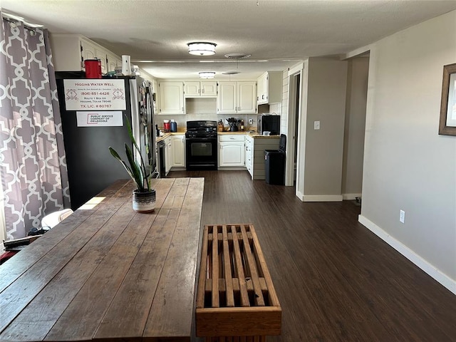 kitchen with black gas range, stainless steel refrigerator, dark wood-type flooring, a textured ceiling, and white cabinets