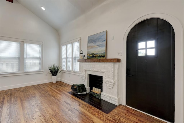 foyer featuring a brick fireplace, a wealth of natural light, lofted ceiling, and hardwood / wood-style flooring