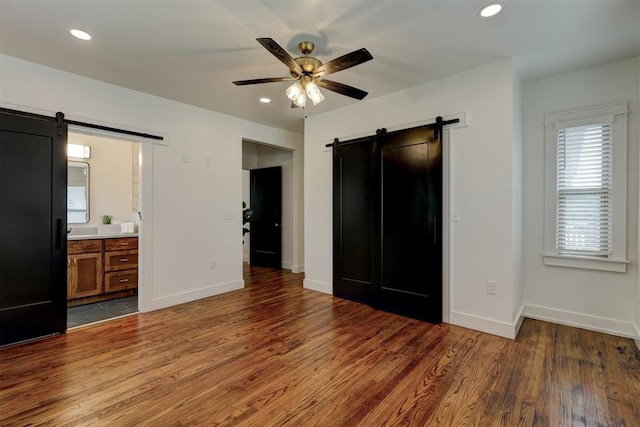 unfurnished bedroom featuring a barn door, ceiling fan, dark hardwood / wood-style flooring, and ensuite bath