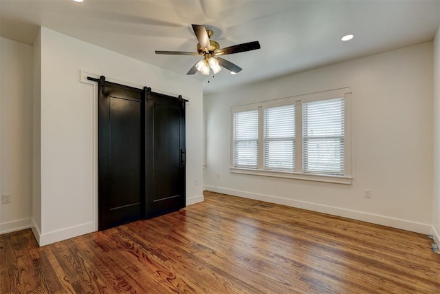 unfurnished bedroom with hardwood / wood-style floors, ceiling fan, and a barn door